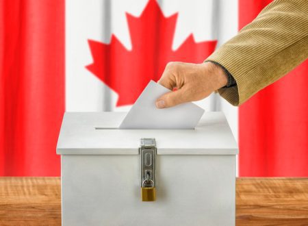 Man putting ballot in ballot box with Canadian flag in background.