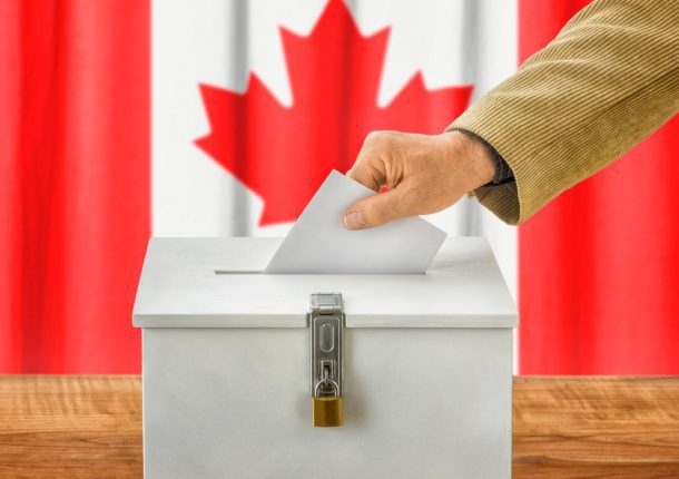 Man putting ballot in ballot box with Canadian flag in background.
